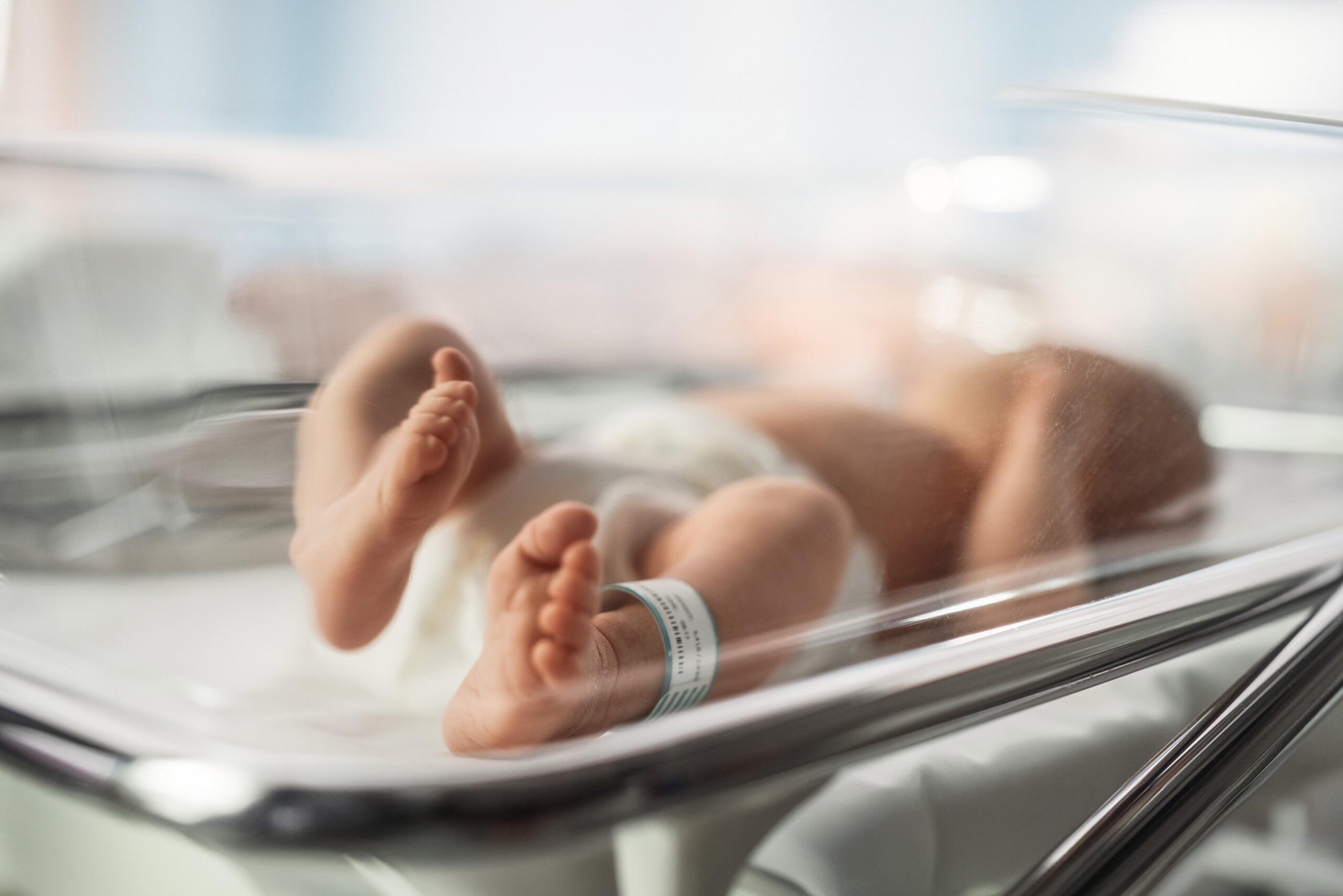 A newborn baby lying in an incubator in a hospital room.