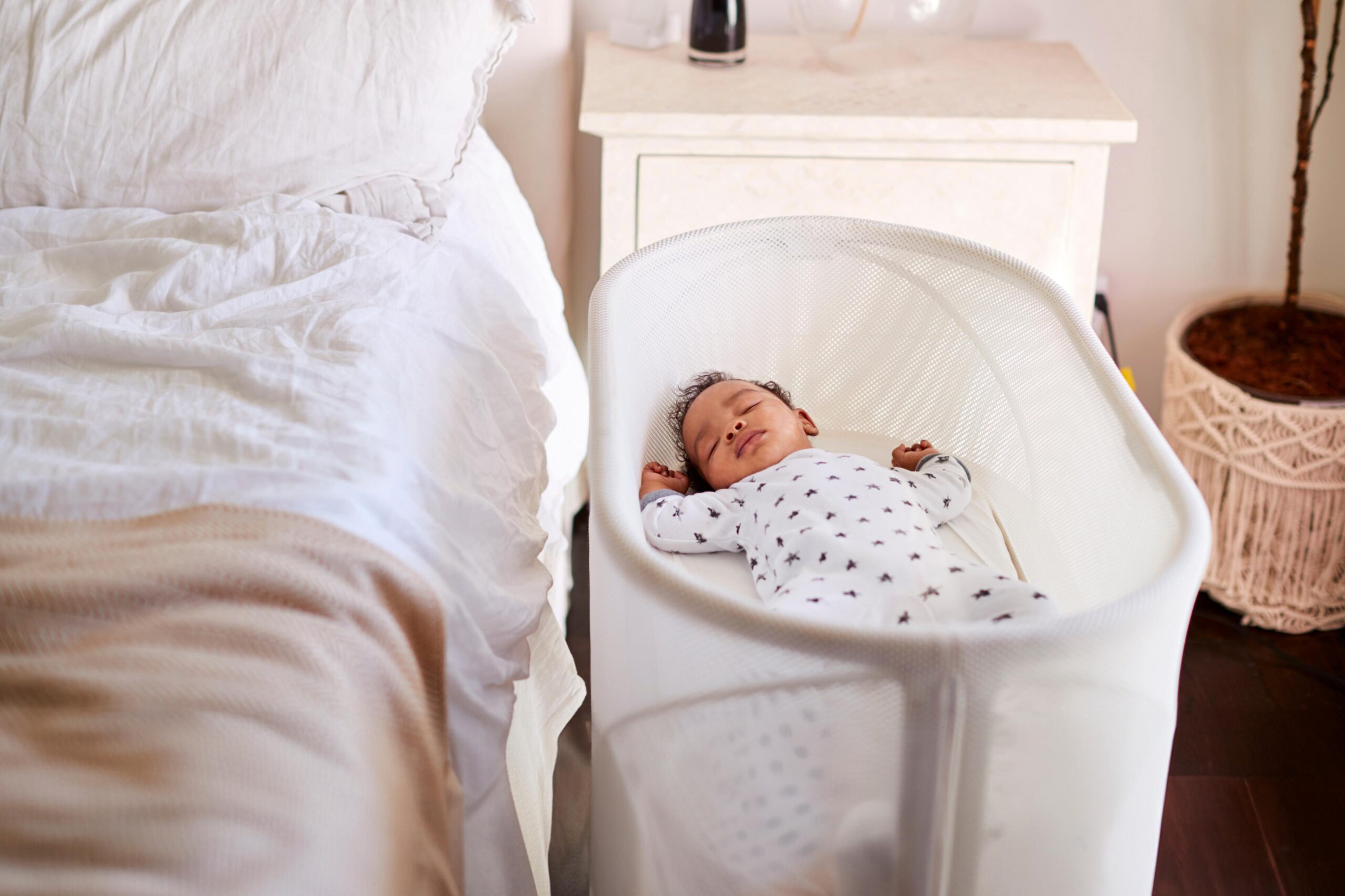 A newborn baby sleeping in a bassinet next to a bed.