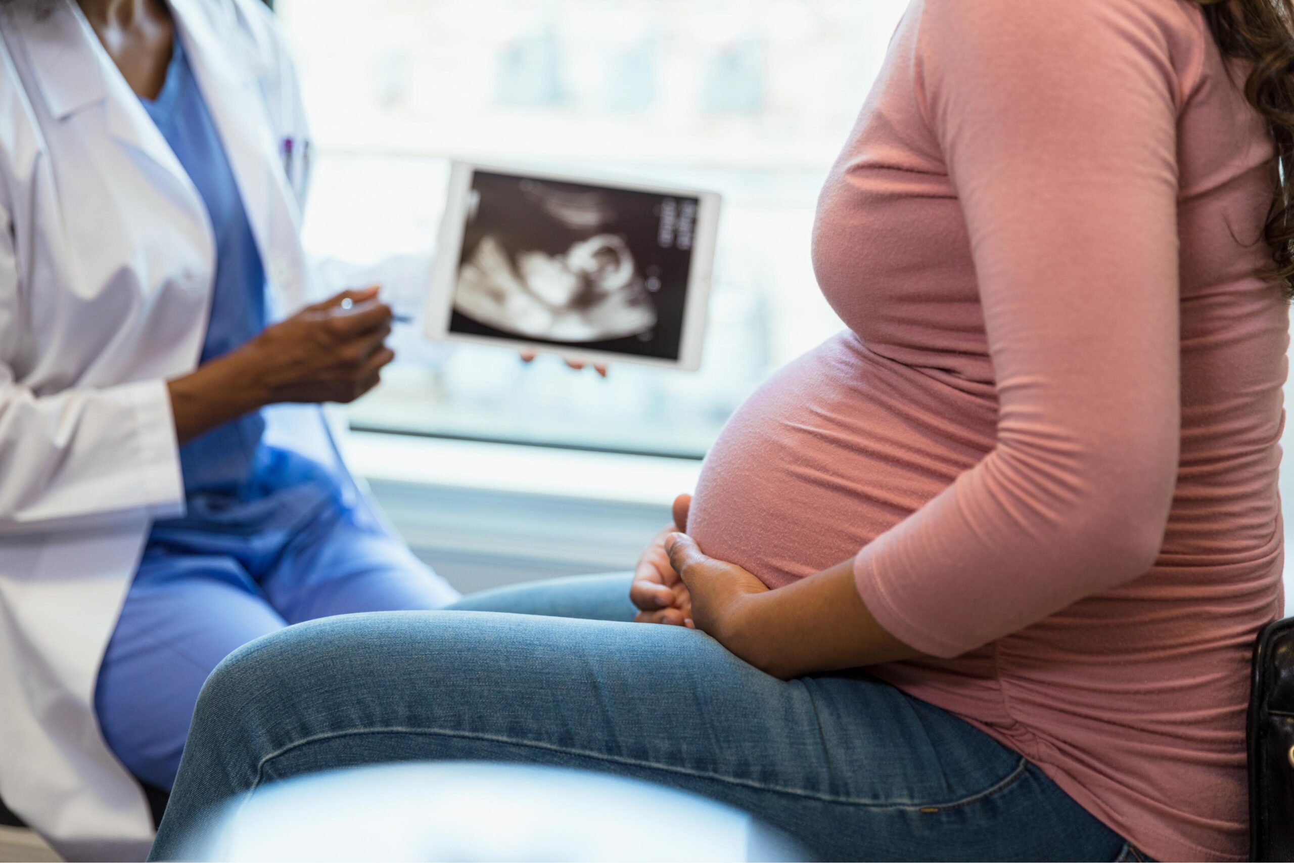 A pregnant woman sitting on a table looking at a sonogram with her doctor.