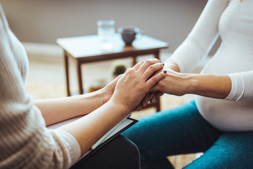 A close-up of a healthcare professional holding the hands of a pregnant woman in a supportive gesture.